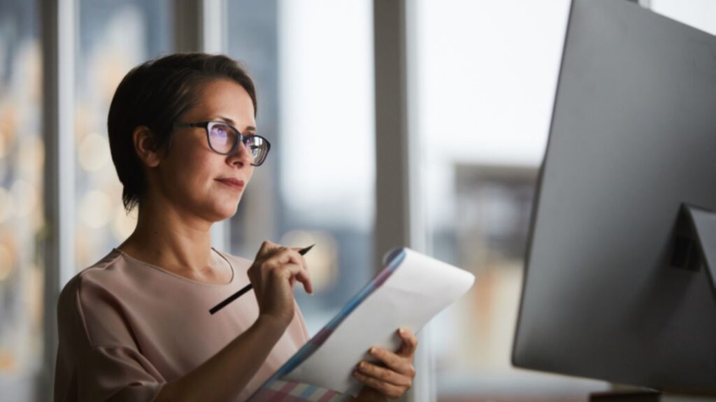 Woman with eyeglasses taking notes in front of Computer